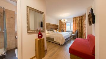 Quarto de hotel com cama, escrivaninha, cadeira, televisão, espelho e chuveiro.