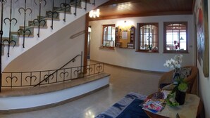 Una imponente escalera con barandillas de metal ornamentadas, vistas al exterior a través de amplios ventanales y un rincón acogedor con una mesa y sillas.