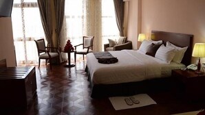 Habitación de hotel con una cama grande, dos sillas, una mesita, televisión y ventana con cortinas.