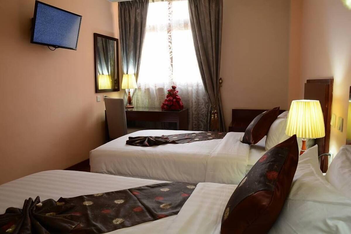 A hotel room with two beds, a TV, a desk with a lamp, and a window with curtains.
