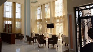 Un vestíbulo amplio con mostrador de recepción, varias zonas de estar y grandes ventanales con cortinas estampadas.