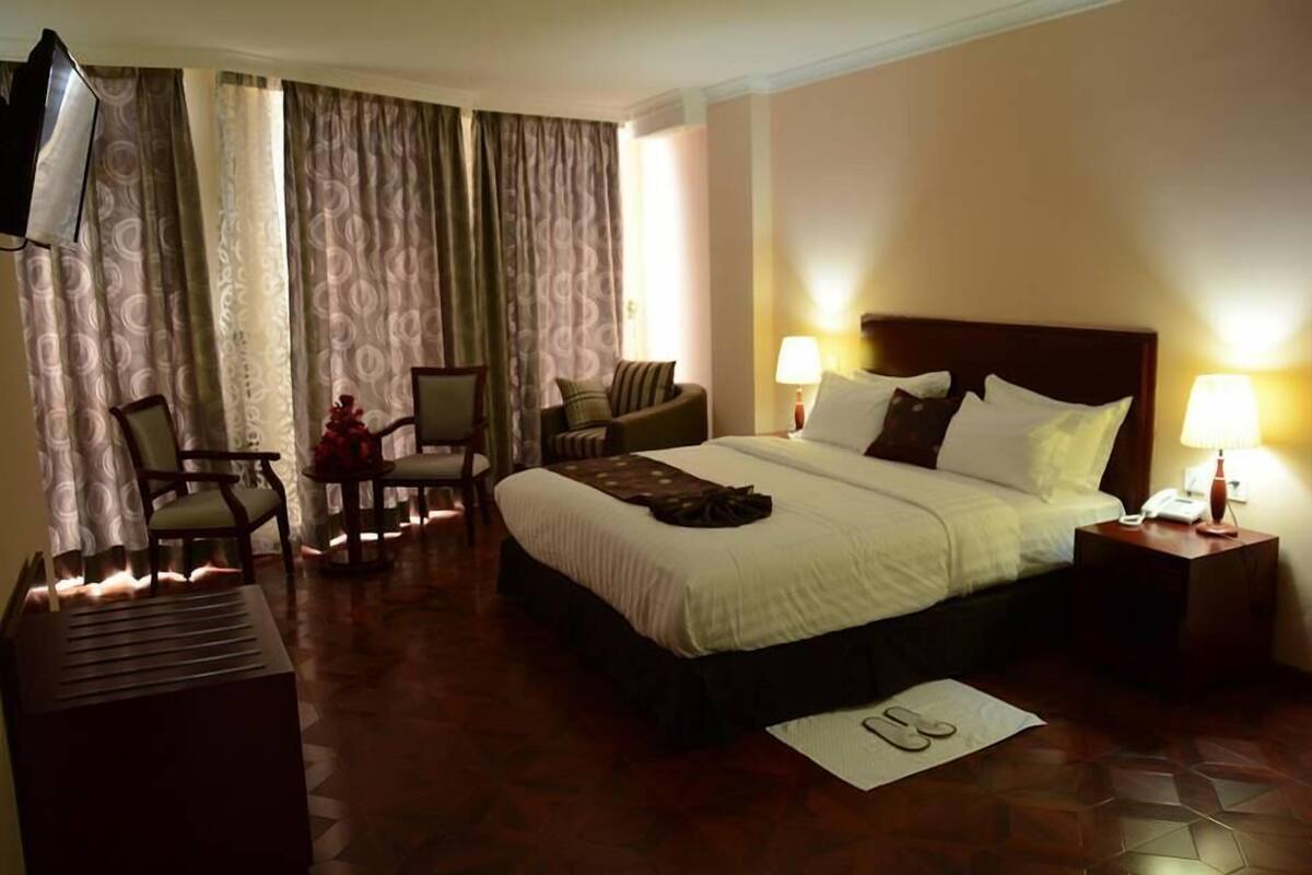 A hotel room with a bed, two chairs, a TV, and a lamp.