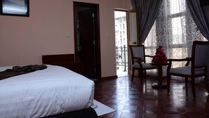Habitación de hotel con cama, una mesa de comedor con sillas, balcón con barandilla y ventana con cortinas.