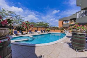A swimming pool with lounge chairs, surrounded by potted plants and a building with balconies. - King David Suites (Noord)