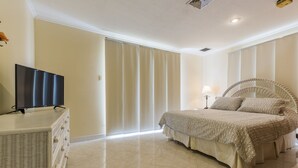 A bedroom with a bed, a television on a dresser, and a large window with curtains. - King David Suites (Noord)