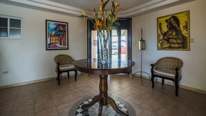 A dining area with a round table, two wicker chairs, a vase with flowers, and two paintings on the walls. - King David Suites (Noord)