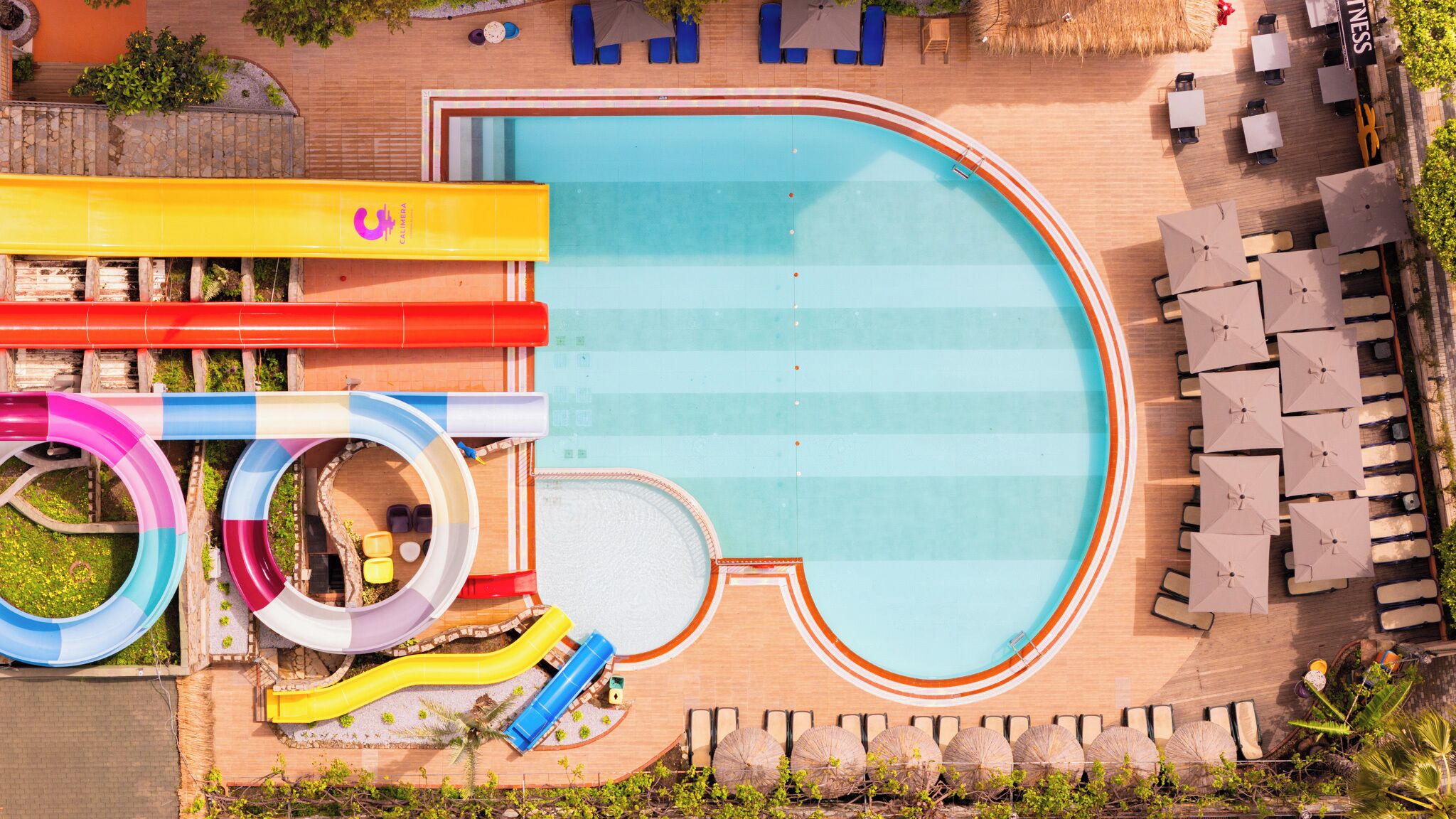 Ein Schwimmbecken mit Wasserrutschen, Liegestühlen und Sonnenschirmen.