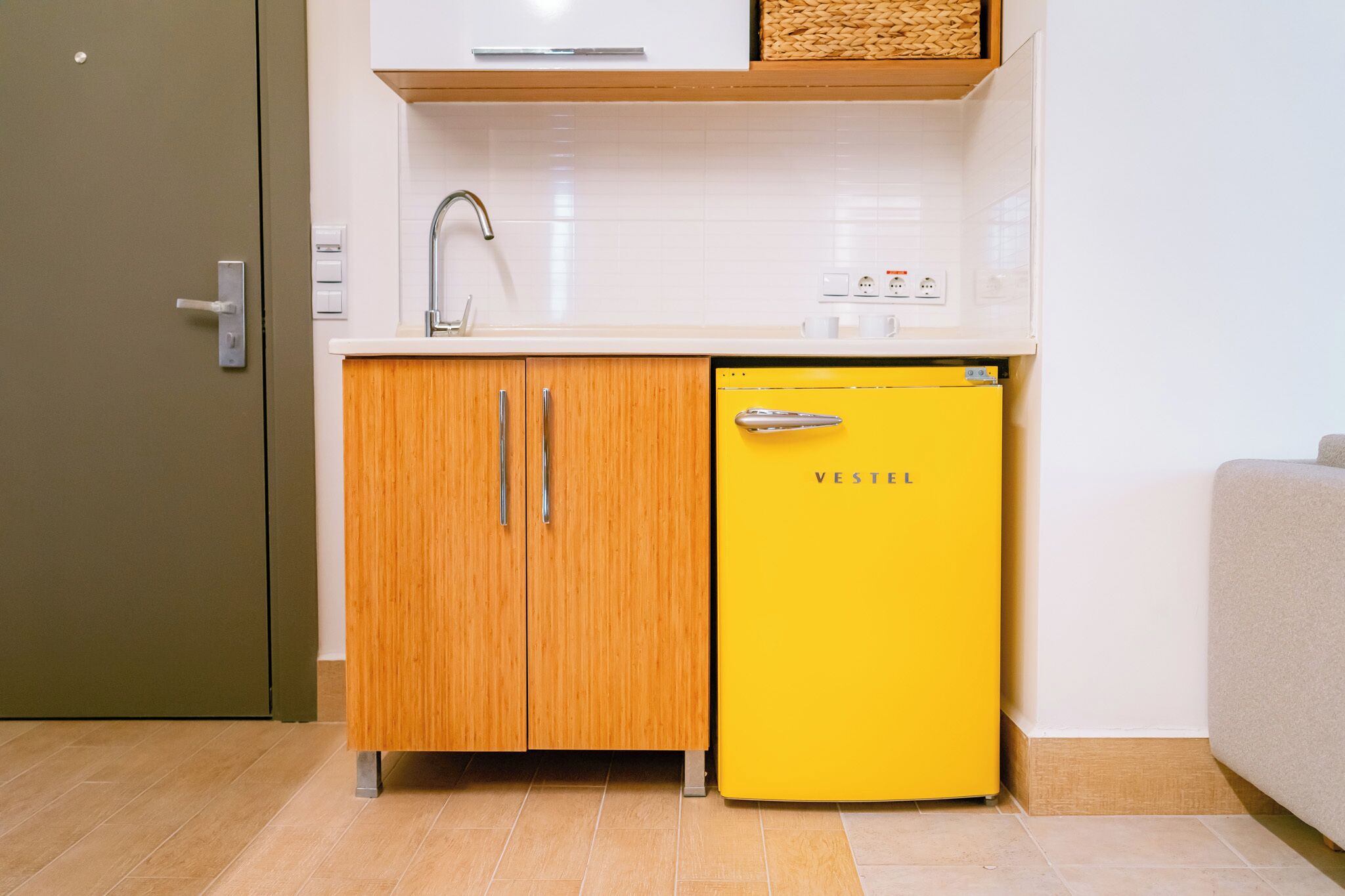 A compact kitchen with a yellow refrigerator, wooden cabinets, a white countertop, and a built-in sink.