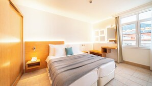 Una camera d'albergo con un letto, comodini, uno specchio, una finestra vista e un armadio in legno.