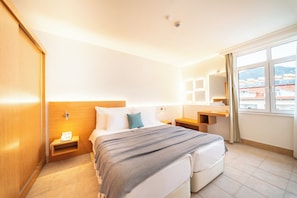 Ett hotellrum med en säng, sängbord, en spegel, ett fönster med utsikt och en garderob i trä.