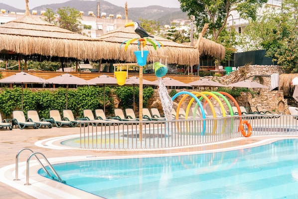 A swimming pool with a water feature, lounge chairs, and thatched umbrellas.
