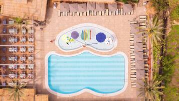 An aerial view of a resort with a swimming pool, lounge areas, and a restaurant.