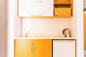 Une cuisine avec des meubles blancs, un plan de travail en bois, une bouilloire en acier inoxydable et un lave-vaisselle.