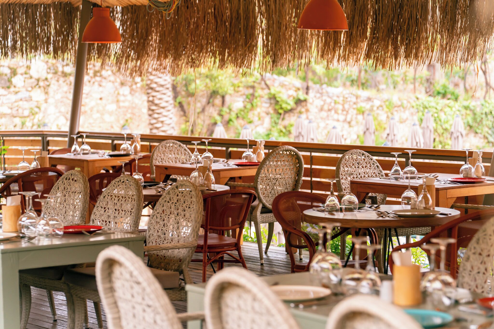 An outdoor restaurant with wicker chairs, round tables, and hanging red lamps.