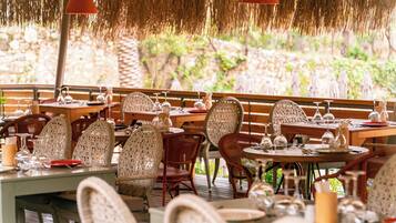 An outdoor restaurant with wicker chairs, round tables, and hanging red lamps.