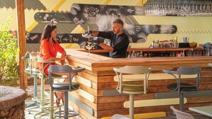 Zona bar con un bancone in legno, sgabelli da bar e una parete decorata con immagini a tema bevande.