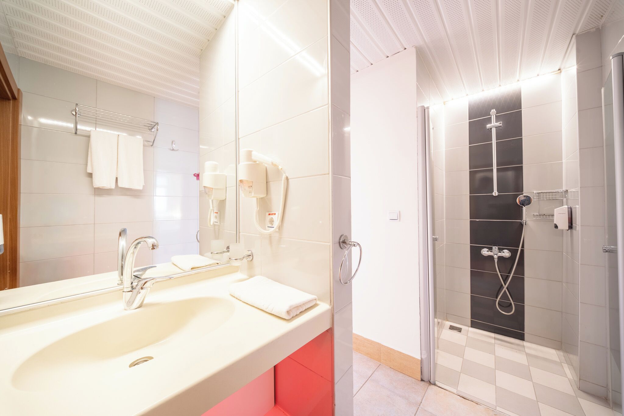 A bathroom with a sink, mirror, towel rack, and a shower area with a glass door.
