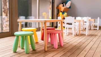 A wooden deck with a table and colorful stools, white chairs, and a large window.