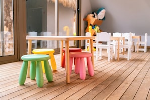 A wooden deck with a table and colorful stools, white chairs, and a large window. - Calimera Sunpark Alanya (Alanya)
