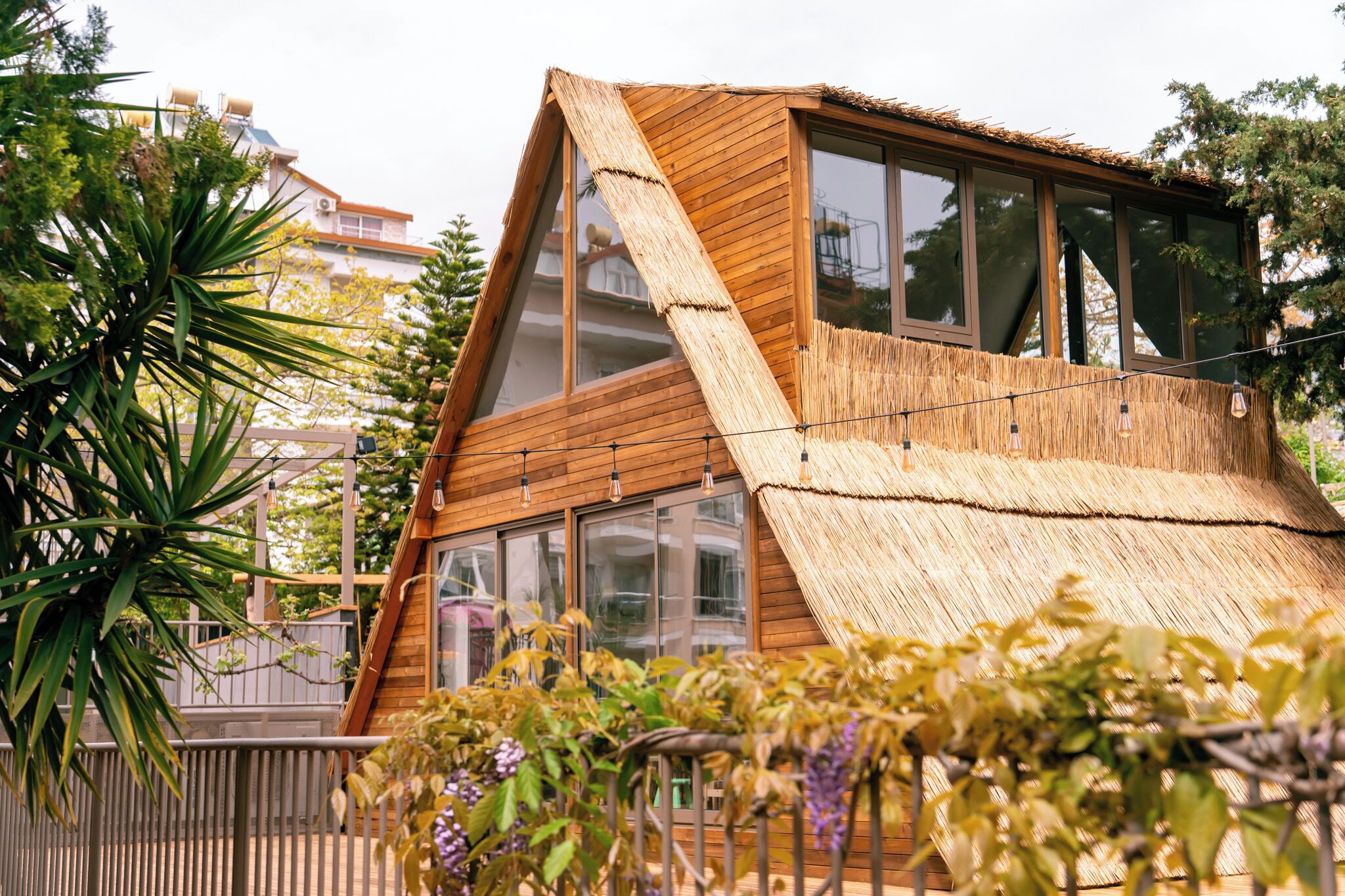 A modern wooden house with large windows and a thatched roof.