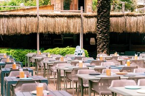 An outdoor dining area with thatched roofs, wicker furniture, and a palm tree. - Calimera Sunpark Alanya (Alanya)