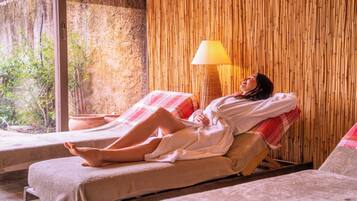 Un cuarto de spa con dos camillas reclinables, un muro de bambú y una ventana que da a zonas verdes.