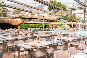 Un espace extérieur aménagé pour les repas, avec des tables et des chaises, une piscine et des parasols en chaume.