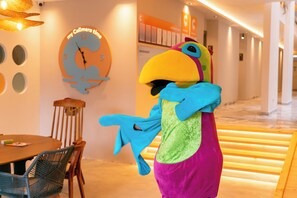 A hotel lobby with a large wall clock, a wooden dining table with chairs, and a colorful mascot. - Calimera Sunpark Alanya (Alanya)