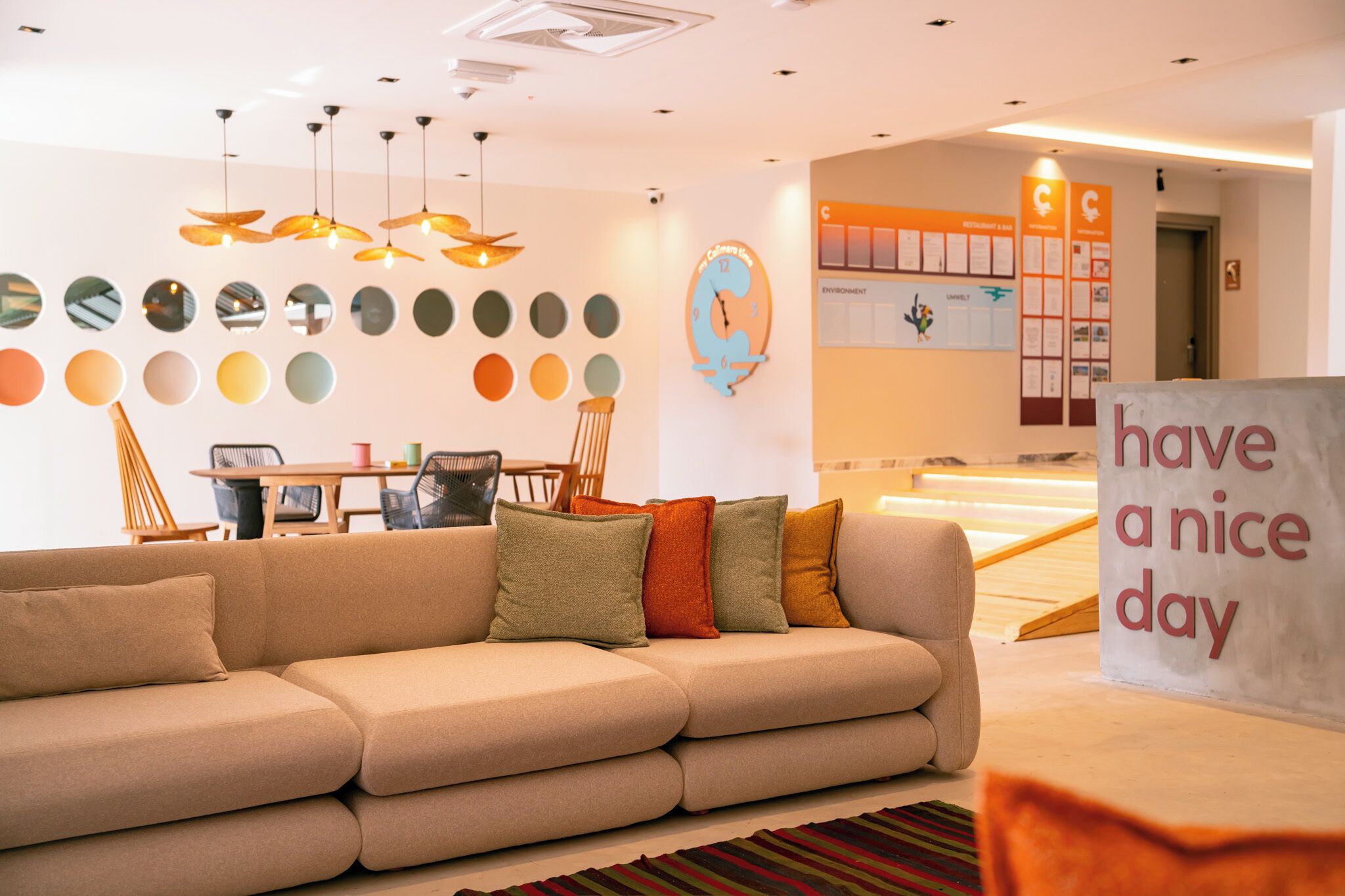 Een modern interieur met een bank, een bordje met de tekst 'have a nice day', een wand met ronde spiegels en een houten tafel met stoelen.
