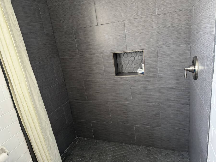 A shower with dark textured tiles, a small window, and a shower curtain.