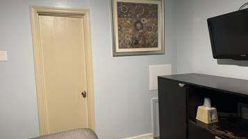 A room with a bed, a black TV on the wall, a framed abstract painting, and a black filing cabinet.