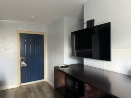Quarto com porta azul escura, televisão de tela plana montada e painel de madeira para entretenimento.