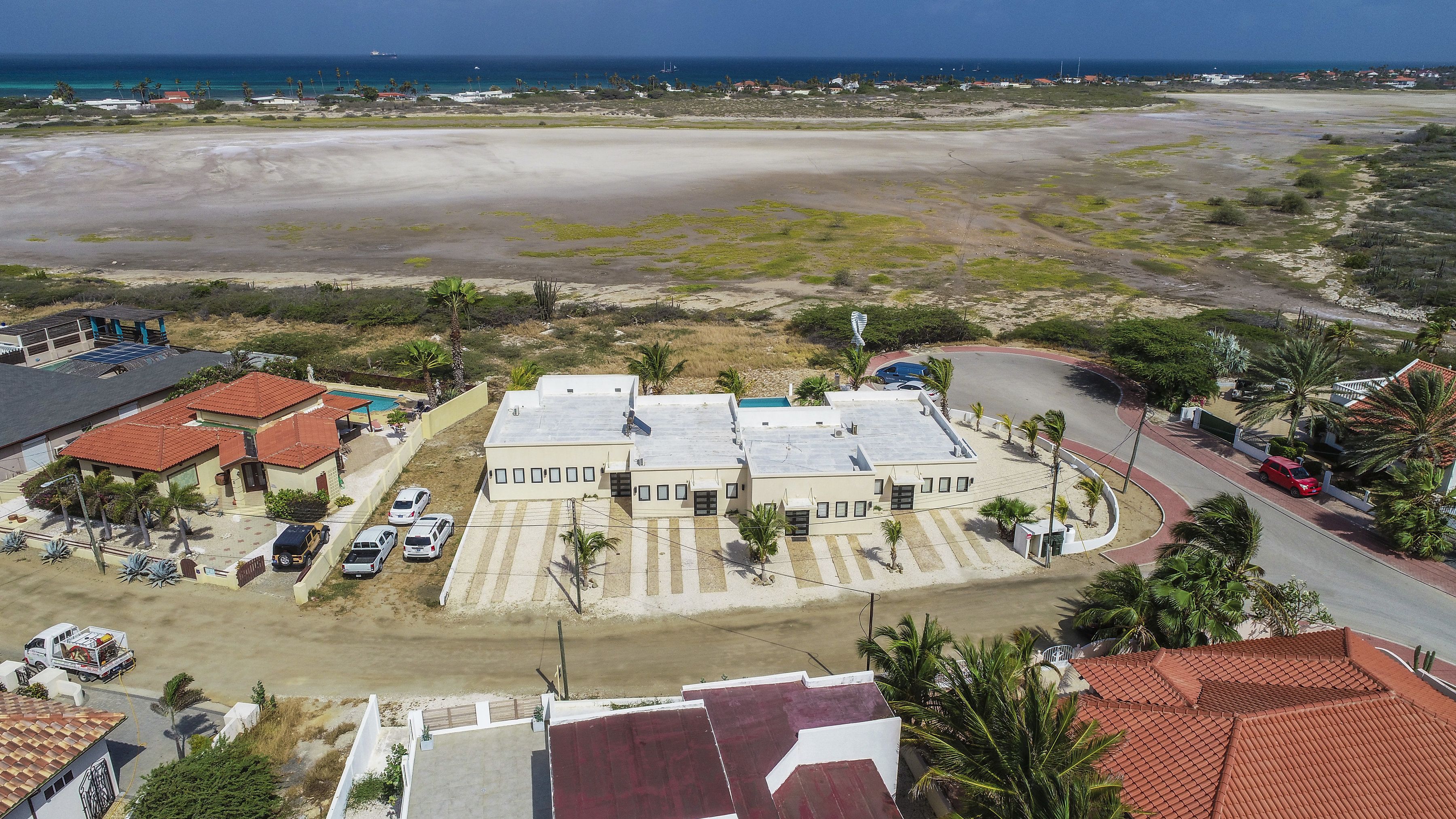 A coastal residential area with a large building complex, a sandy beach, and a clear view of the ocean.