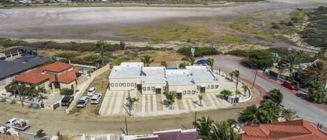 A coastal residential area with a large building complex, a sandy beach, and a clear view of the ocean.