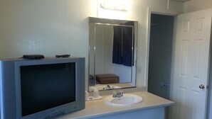 A bathroom with a television mounted on the wall, a sink, and a mirror above it. - Americana Motel (Avenel)