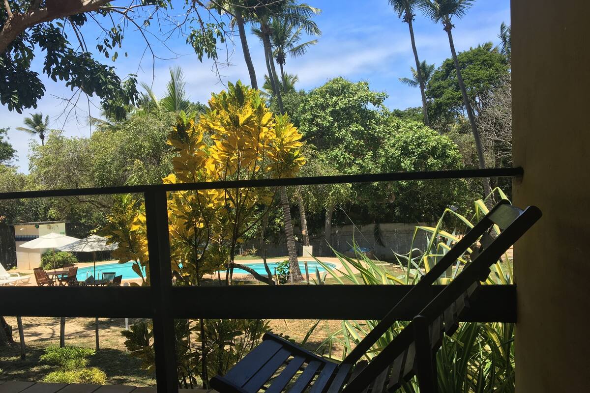 Un balcón con vista a una piscina, palmeras y una silla.