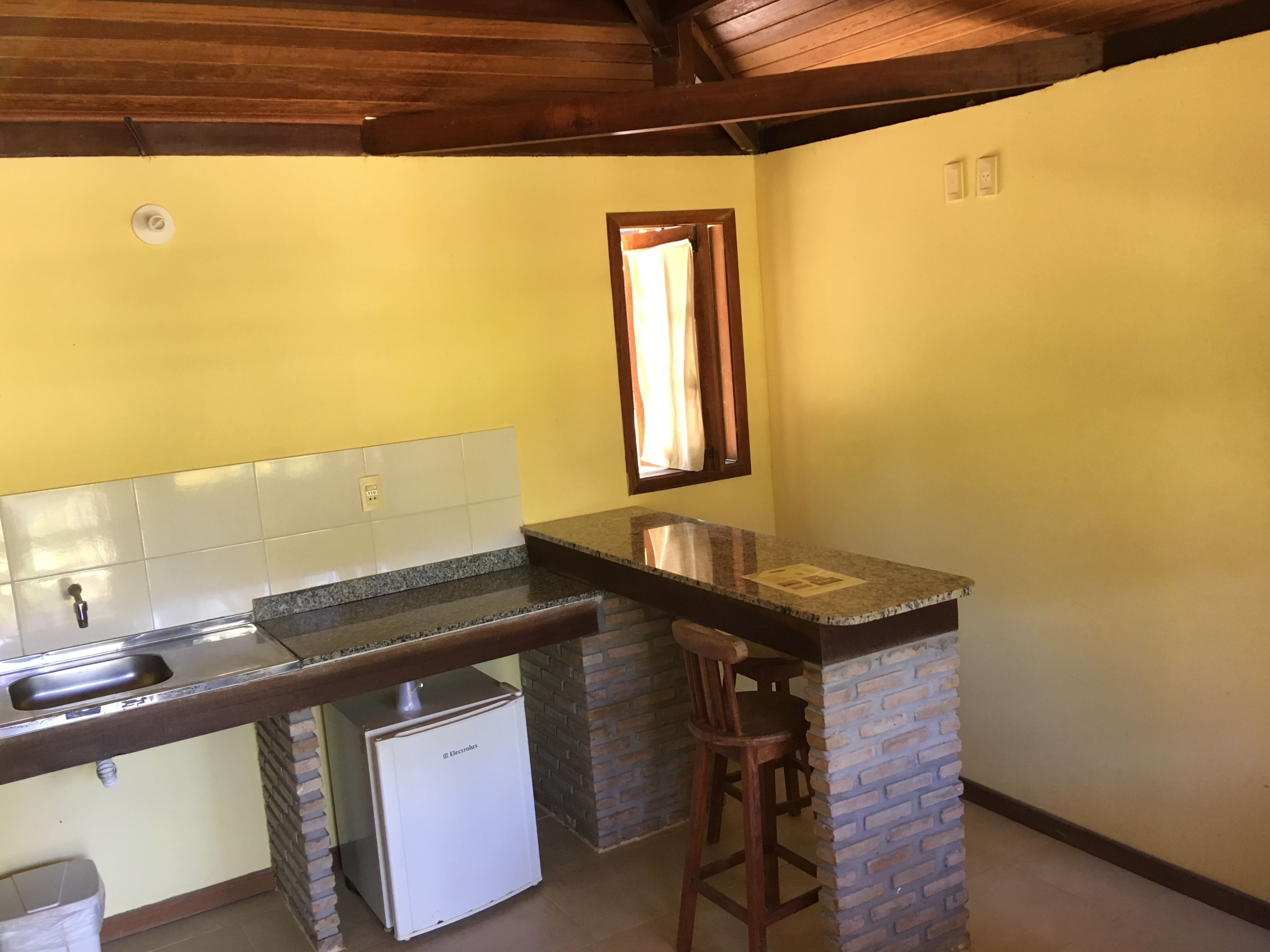 Una cocina compacta con encimera de granito, un refrigerador pequeño y una ventana con cortinas.