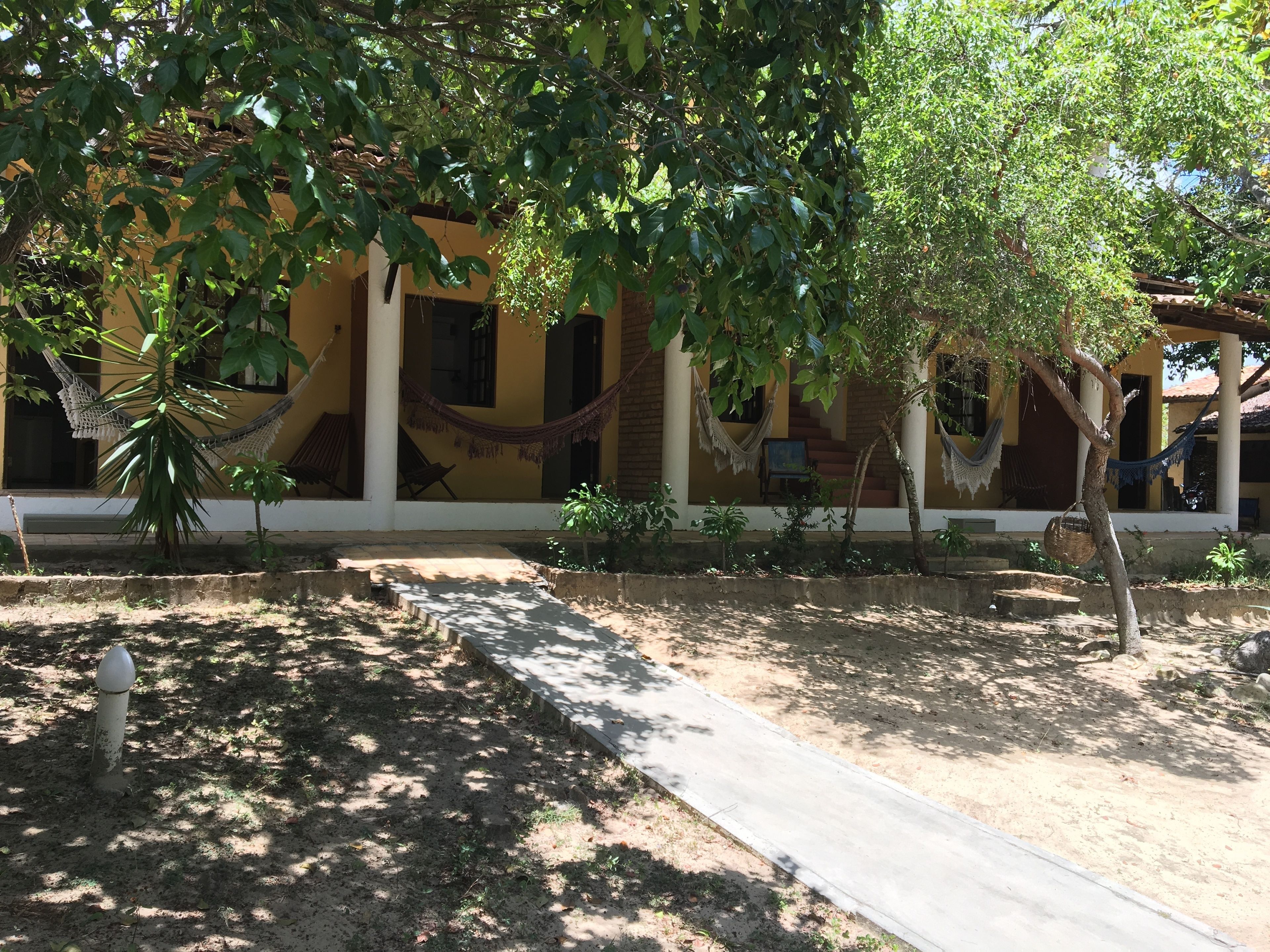 A yellow building with a covered porch, hammocks, and a concrete pathway.