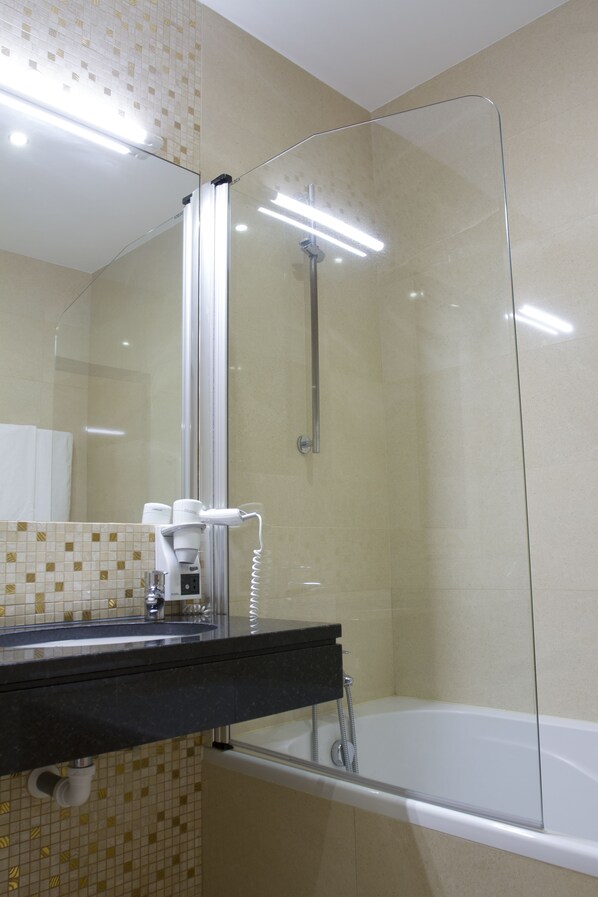 A modern bathroom with a glass-enclosed shower, a black countertop, and a white bathtub.