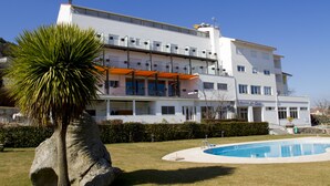 Un hôtel à plusieurs étages doté d’une piscine, d’un palmier et d’une pelouse bien entretenue.