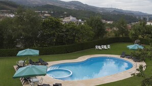 Une piscine entourée de chaises longues et de parasols, elle-même bordée d’une pelouse bien entretenue et d’arbres.
