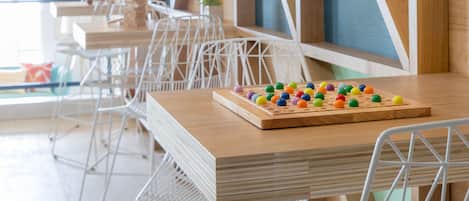 Un comedor moderno con mesas de madera y sillas metálicas, paredes de madera con patrones geométricos e iluminación colgante.