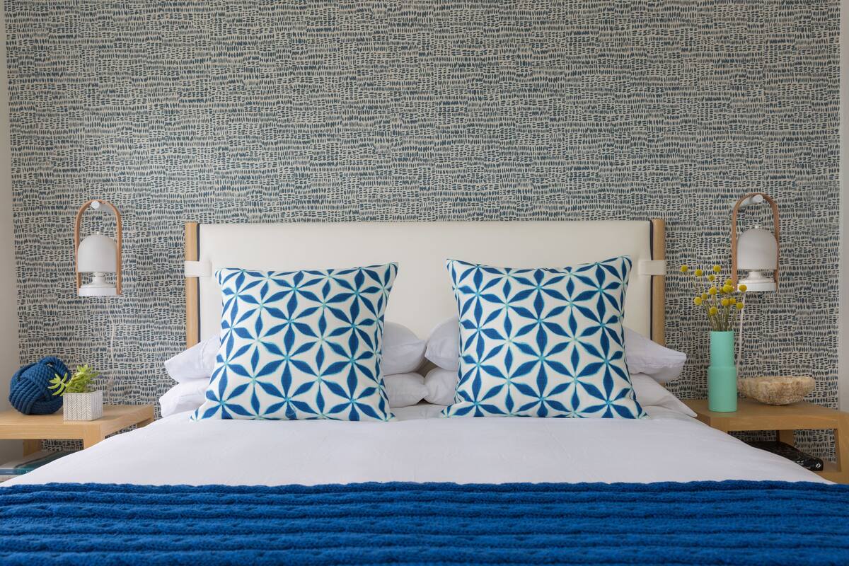 A bed with a white headboard, two pillows with a geometric pattern, and a blue blanket.