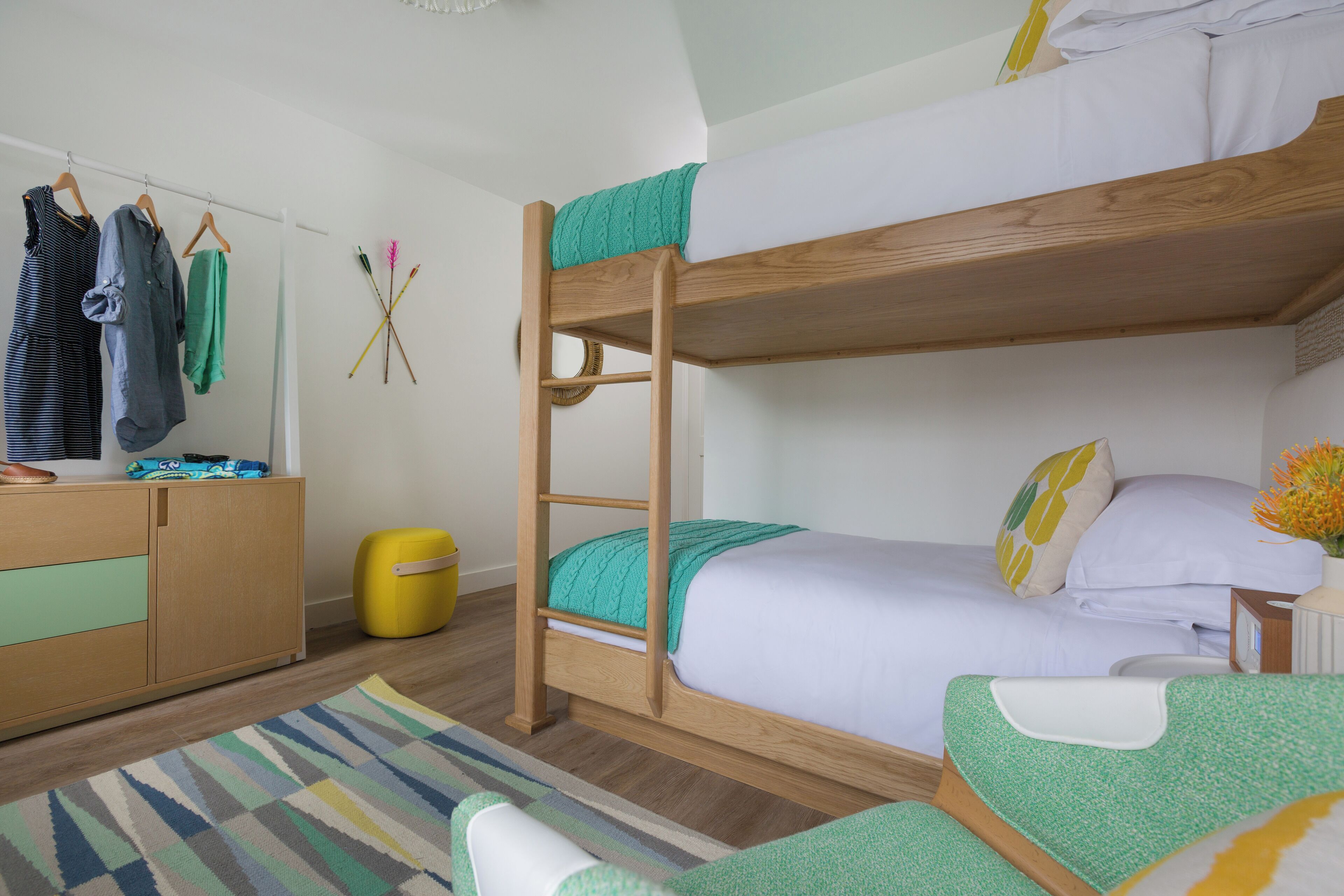 Une chambre avec un lit superposé en bois, une petite table de chevet, une chaise, une armoire et un tapis rayé aux couleurs vives.