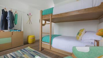 Une chambre avec un lit superposé en bois, une petite table de chevet, une chaise, une armoire et un tapis rayé aux couleurs vives.