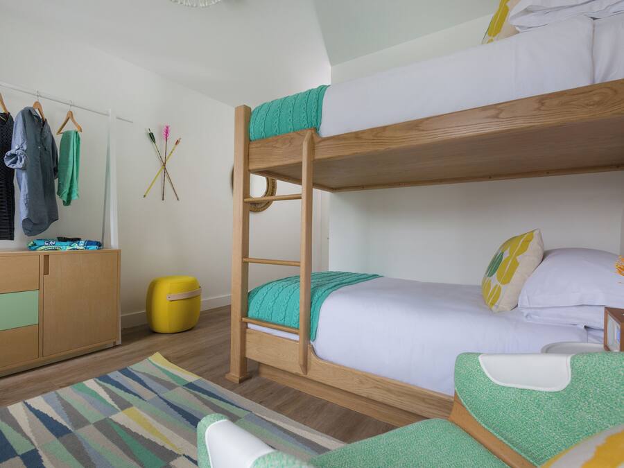 Une chambre avec un lit superposé en bois, une petite table de chevet, une chaise, une armoire et un tapis rayé aux couleurs vives.