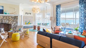 A spacious living room with a stone fireplace, a large window with a view, and a play area for children. - Summercamp (Oak Bluffs)