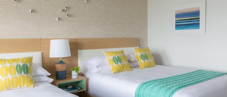 A hotel room with two beds, a headboard, a nightstand with a lamp, and a framed picture on the wall.