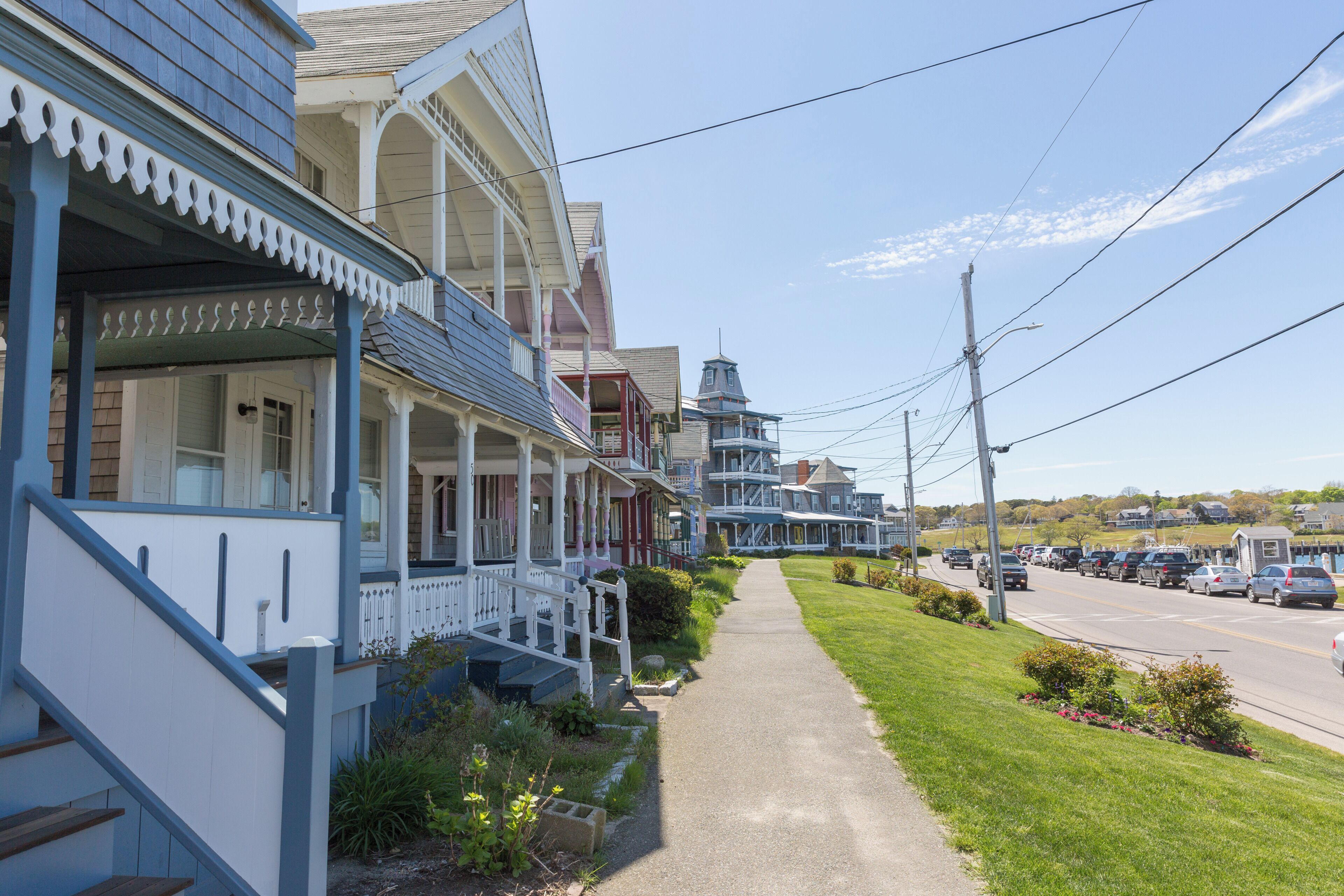 A row of traditional houses with front porches, a sidewalk, and a street with parked cars.