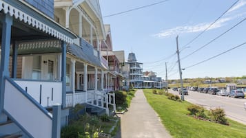A row of traditional houses with front porches, a sidewalk, and a street with parked cars.